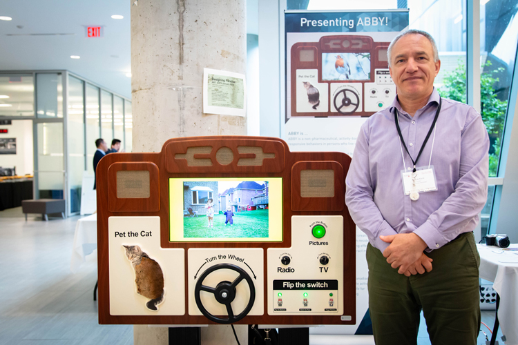 A man stands beside ABBY, an interactive machine that allows people to pet a cat, drive a car wheel, watch videos and listen to the radio.