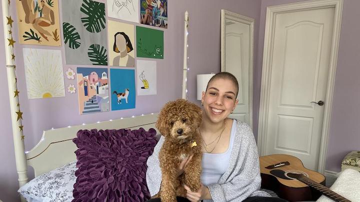 Julia Aprile sits on her bed with a her dog, a small doodle