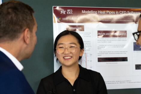an undergraduate researcher smiles as they share their research with two attendees