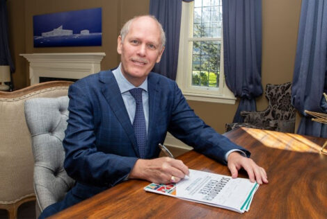 David Farrar in a suit sitting at a desk with papers and a pen. The cover page says