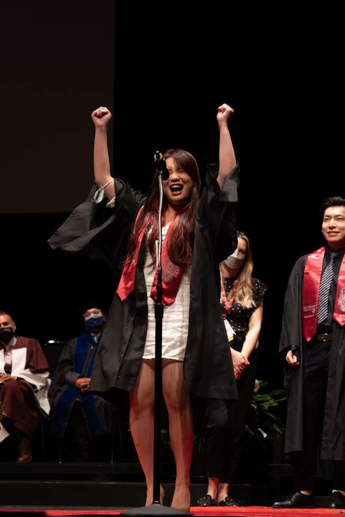 A graduate celebrates on stage with their arms in the air.
