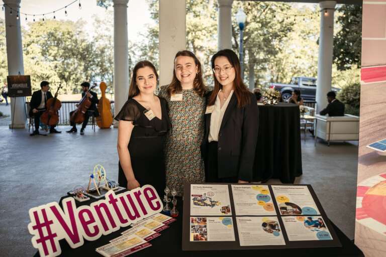 Three people stand behind a Venture booth.
