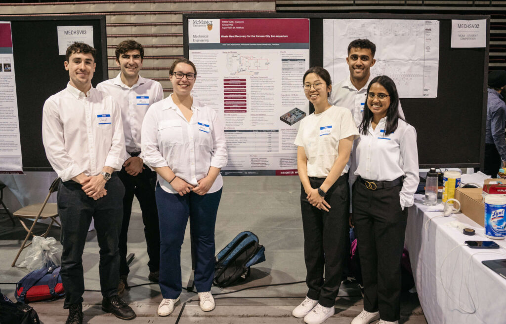 six people in white shirts and black pants posing in front of a presentation board at a student showcase. 