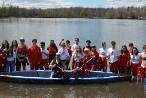 group shot of a team of students standing in the shallow end of a lake surrounding a concrete canoe.