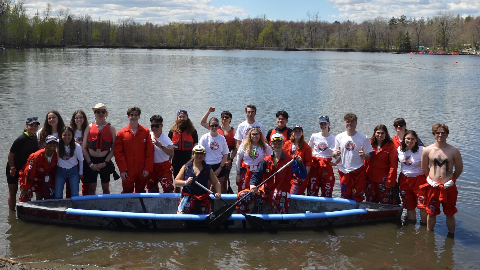 group shot of a team of students standing in the shallow end of a lake surrounding a concrete canoe.