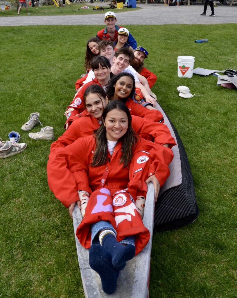 a group of students wearing red jumpsuits posing in a concrete canoe. 