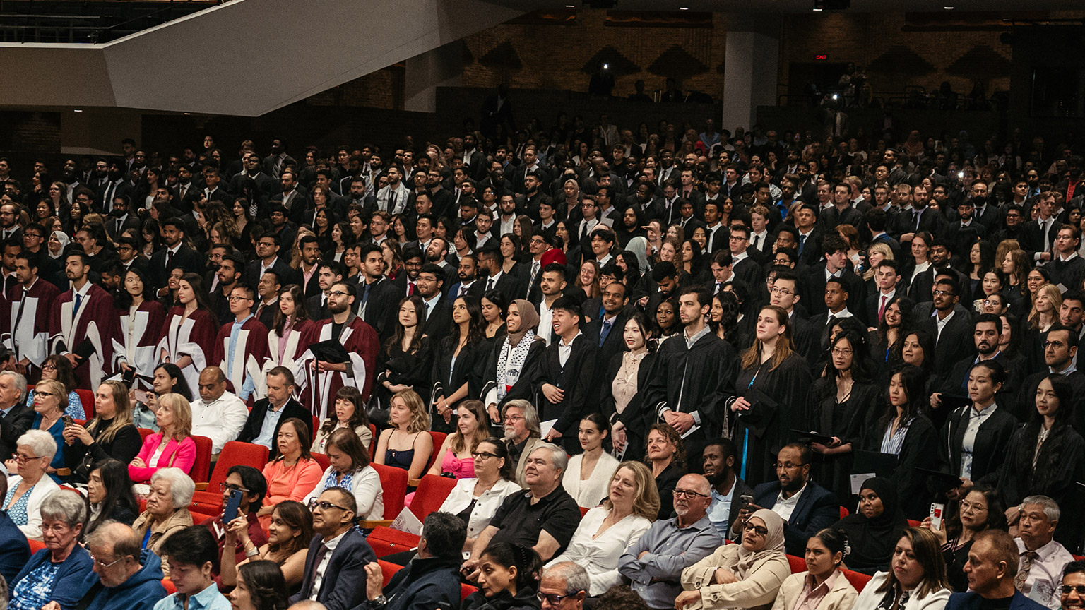 Rows of graduates stand in the seats of First Ontario Concert Hall
