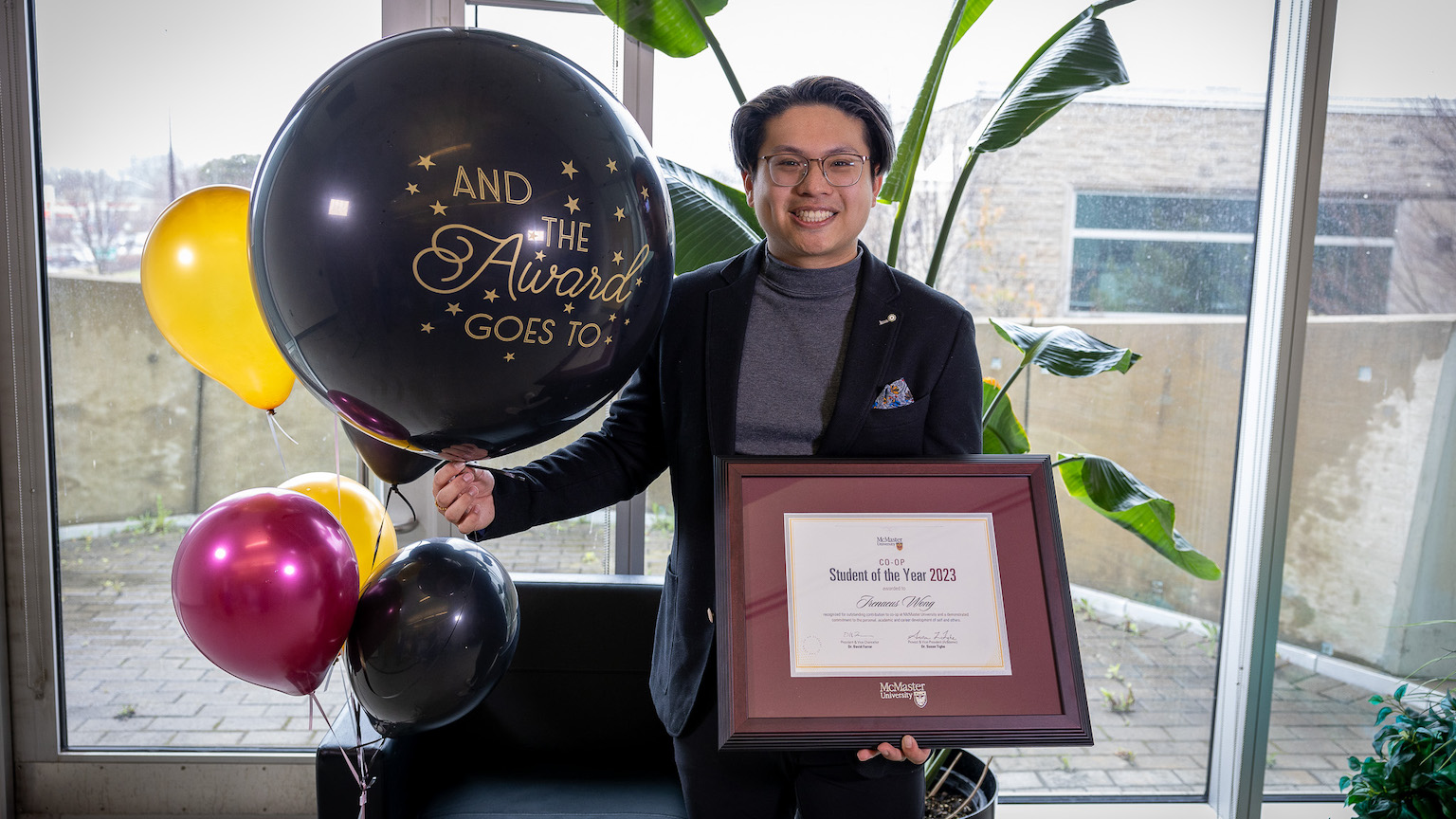 man holding a framed award and a bouquet of balloons.