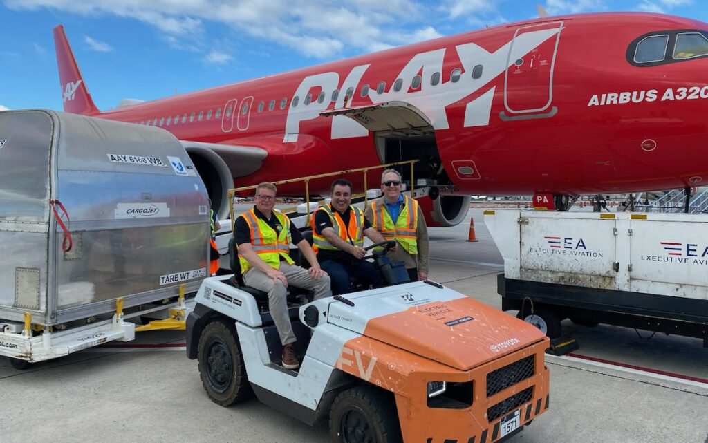 three men in safety vests sitting on a golf cart in front of a commercial airplane.