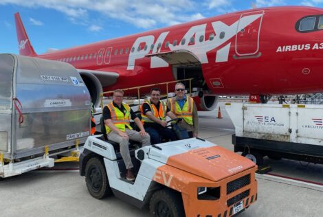 three men in safety vests sitting on a golf cart in front of a commercial airplane.