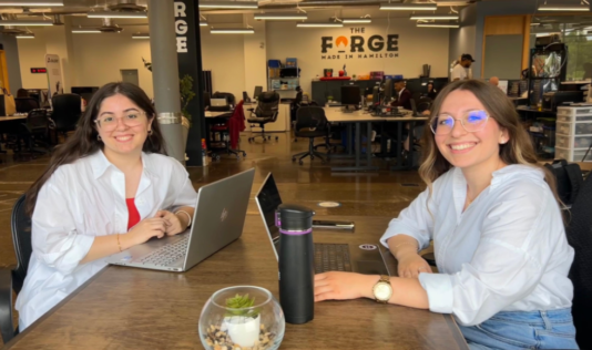 Two McMaster students in The Forge on campus. The space's name is written in the background on the wall.