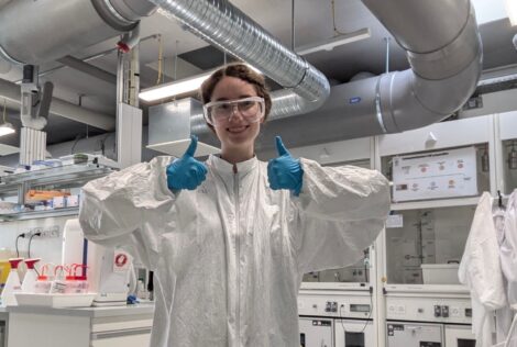 a woman in a lab wearing a clean suit, safety goggles and blue gloves.