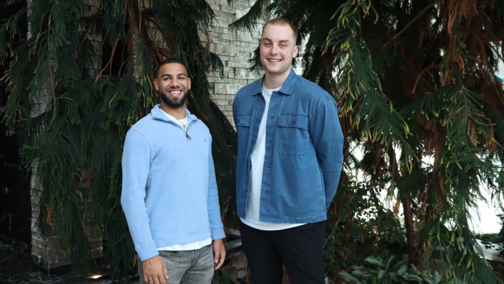 Two men standing in front of pine trees.