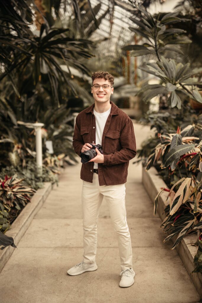 Geoff Shaw Smiling with his camera. Plants are in the back drop