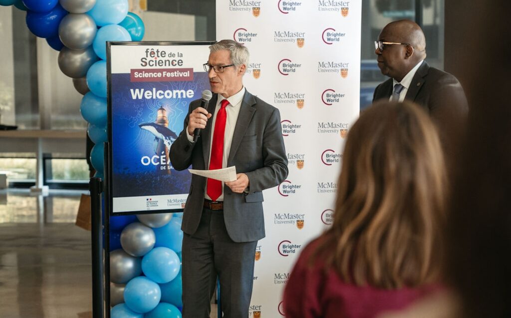 man standing up beside another man at an event holding a microphone.