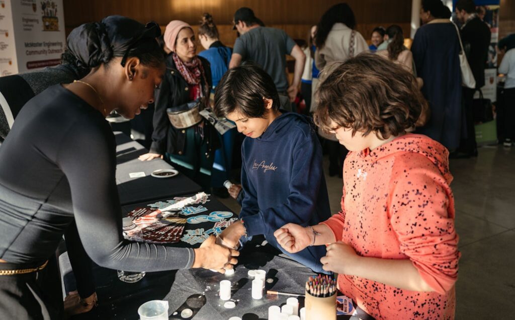 students at a science experiment table with an adult showing them how to complete an experiment.