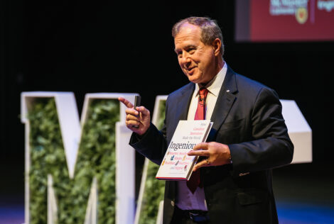 Tom Jenkins on stage holding his book Ingenious.