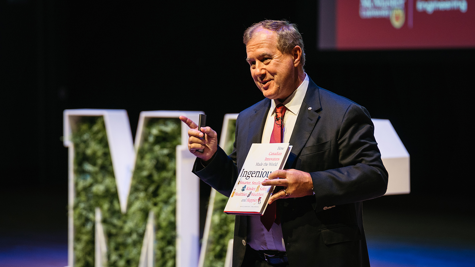 Tom Jenkins on stage holding his book Ingenious.