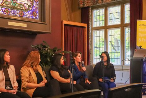 a panel of women sitting on a stage. One of them is holding a microphone and speaking into it.