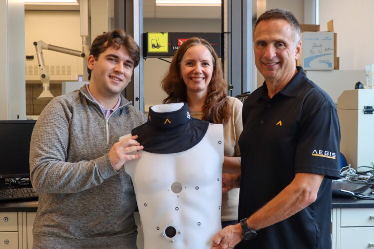 Carson Breweer, Cheryl Quenneville and Joe Camillo hold a mannequin torso that wears a hockey neck guard.