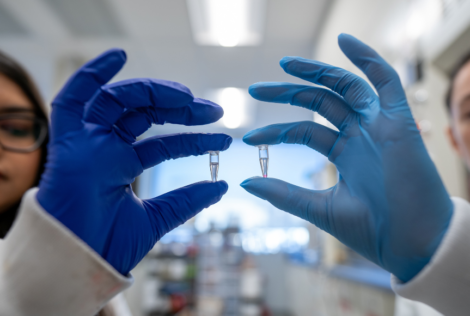 two gloved hands holding up 2 vials of clear liquid,