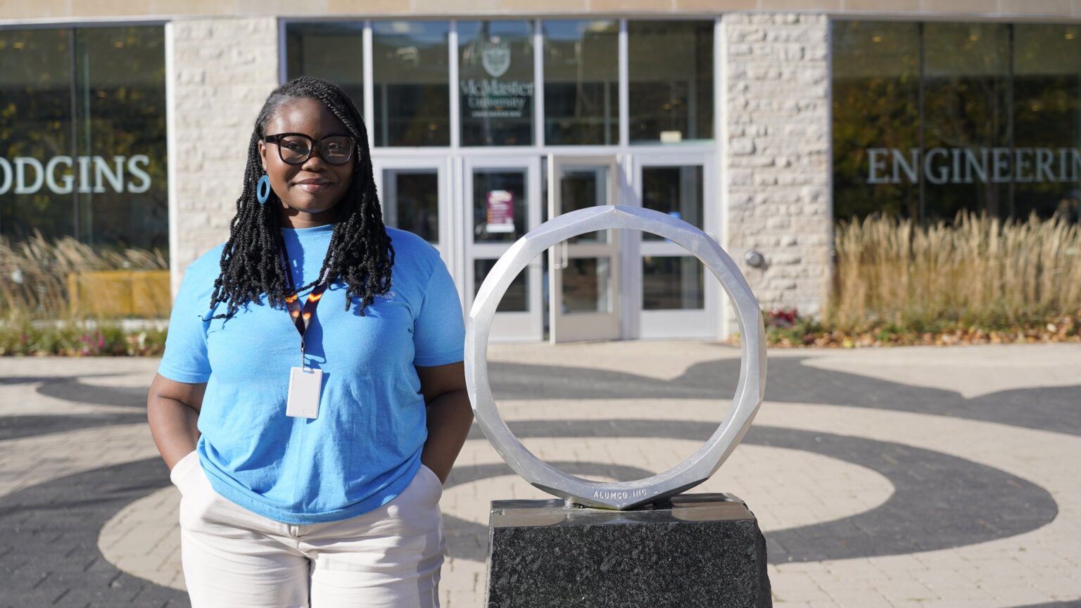 a girl in a blue t-shirt standing beside an iron ring statue.