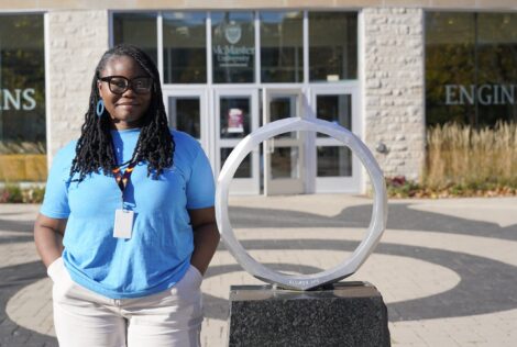 a girl in a blue t-shirt standing beside an iron ring statue.