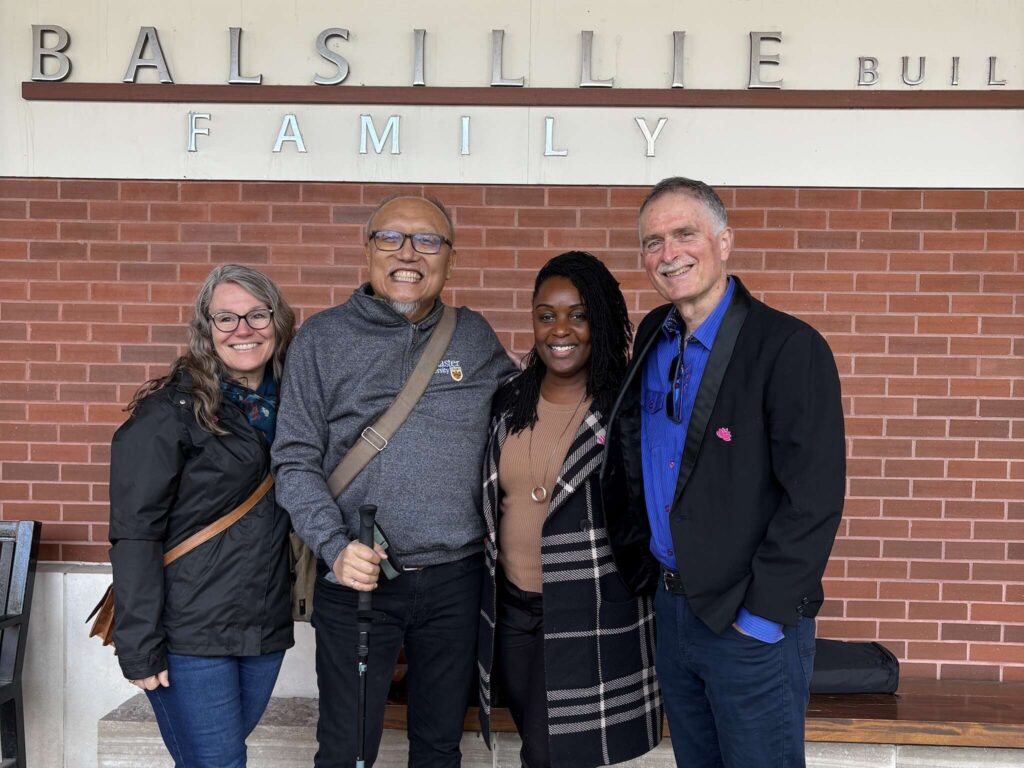 four people posing together in front of building.