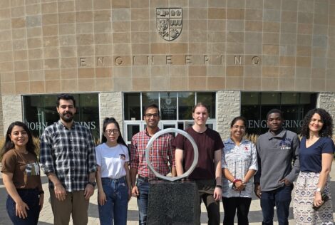 group of people posing behind an iron ring statue in front of an engineering building.