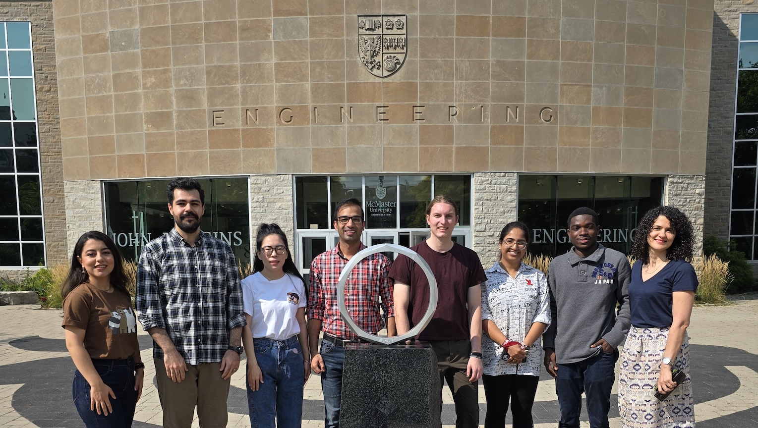 group of people posing behind an iron ring statue in front of an engineering building.